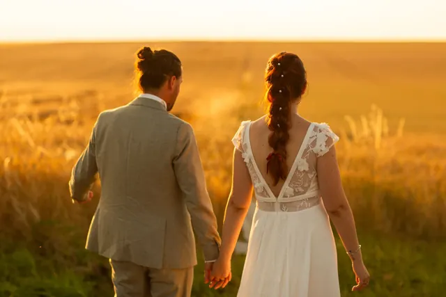 Mariés main dans la main dans un champ de blé à l'heure dorée – Frédéric Leroux, photographe de mariage à Reims