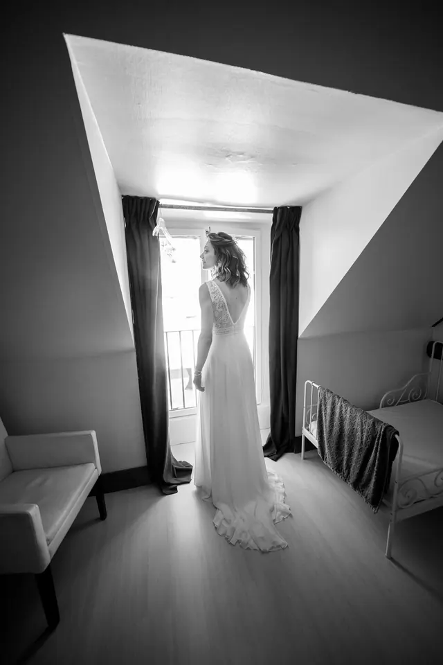 Mariée dans la lumière d'une lucarne, en noir et blanc – Frédéric Leroux, photographe de mariage à Reims